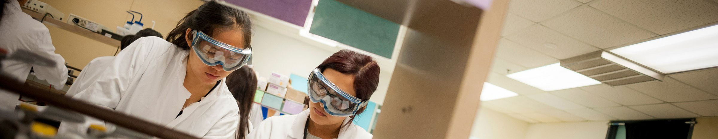 Two students wearing goggles working in a lab