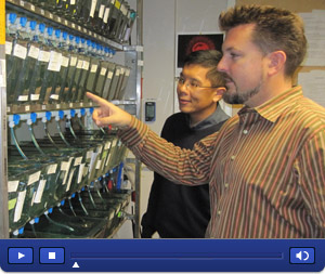 Side photo of David Traver and Neil Chi looking at rows of zebrafish tanks