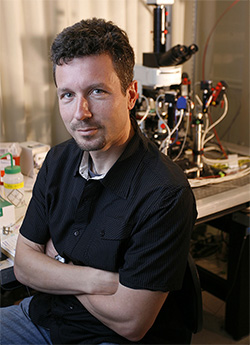 Massimo Scanziani sitting in a chair crossing his arms in front of a table with lab equipment on it
