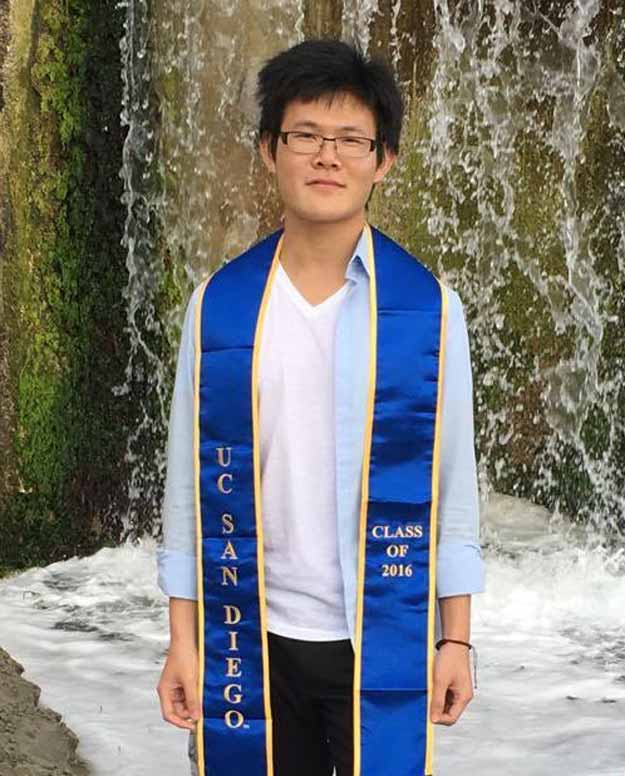man wearing UCSD graduation stole and standing in from of waterfall 