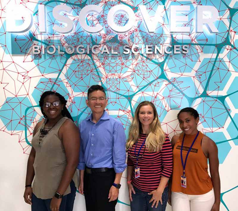 Four people lined up to have their photo taken in front of a wall motif