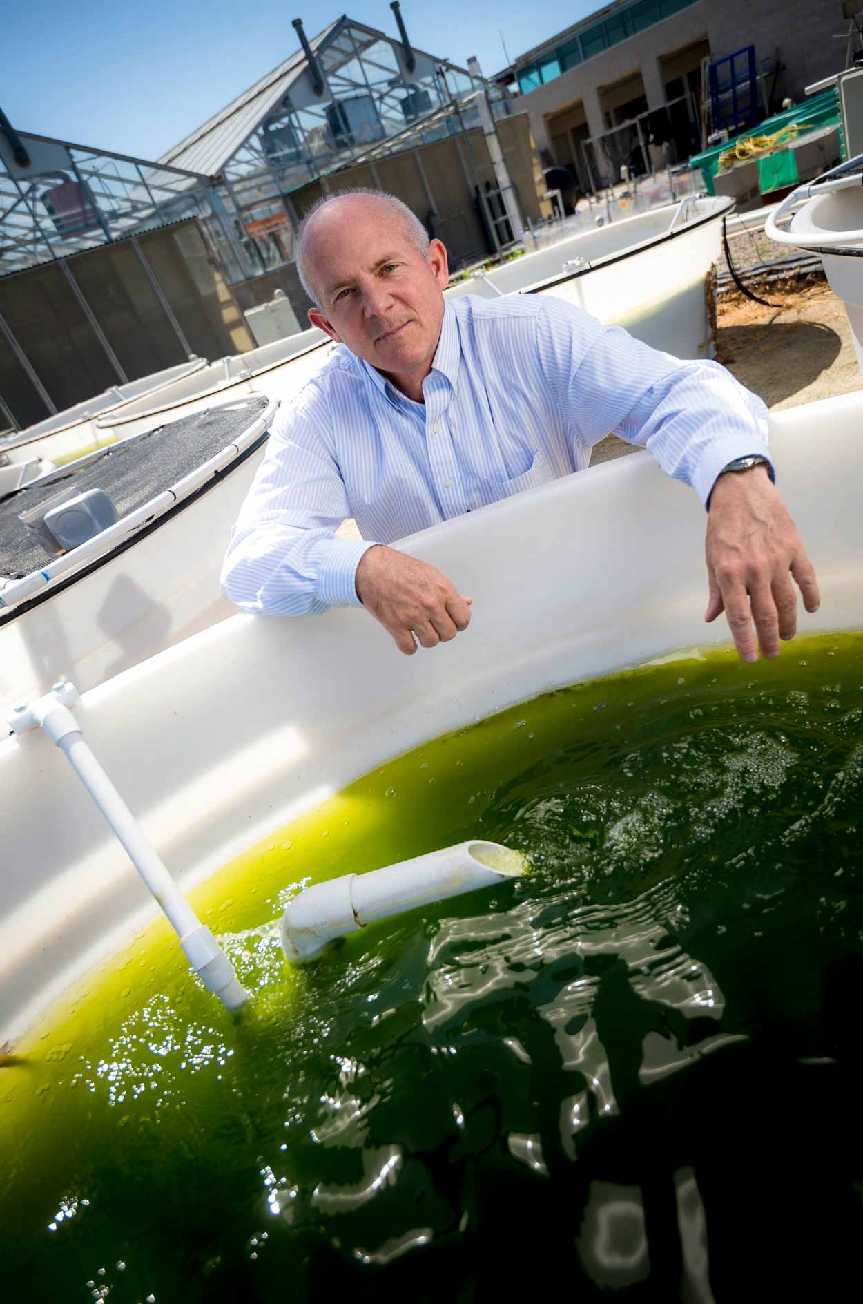 Stephan Mayfield posing for a photo with large outdoor bio-algae tanks
