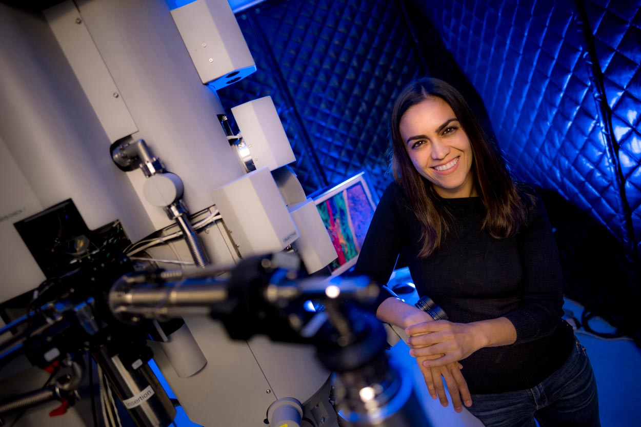 Brunette woman (Elizabeth Villa) standing next to a telescope in a lab